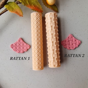 May include: Two beige rolling pins with rattan patterns, and two pink rattan-patterned shapes. The text "RATTAN 1" and "RATTAN 2" are printed below the shapes. The items are arranged on a grey surface.