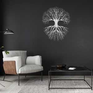 May include: A silver metal tree of life wall art decor. The tree design features a symmetrical arrangement of branches and roots. The artwork is mounted on a dark gray wall, creating a striking contrast. The room also includes a modern armchair, a coffee table, and a rug.