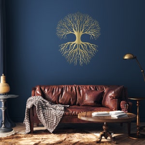 May include: A gold-colored tree of life wall art decorates a dark blue wall. The tree design features a circular crown of branches and roots. A brown leather sofa with pillows and a blanket sits below the artwork. A round wooden coffee table and a floor lamp are also in the room.
