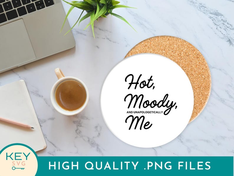 May include: A white ceramic coaster with the text "Hot, Moody, and Unapologetically Me" in black script. The coaster sits on a cork base. A cup of coffee, a laptop, a notepad, and a pencil are also visible.