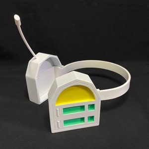 Può includere: Auricolare in plastica bianca con un design giallo e verde. L'auricolare ha un microfono attaccato all'auricolare sinistro.