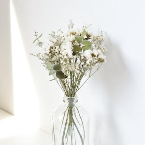 May include: A bouquet of dried white flowers with green stems in a clear glass vase.