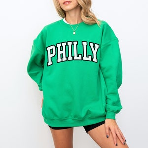 May include: A green sweatshirt with the word "PHILLY" printed in white letters with a black outline.