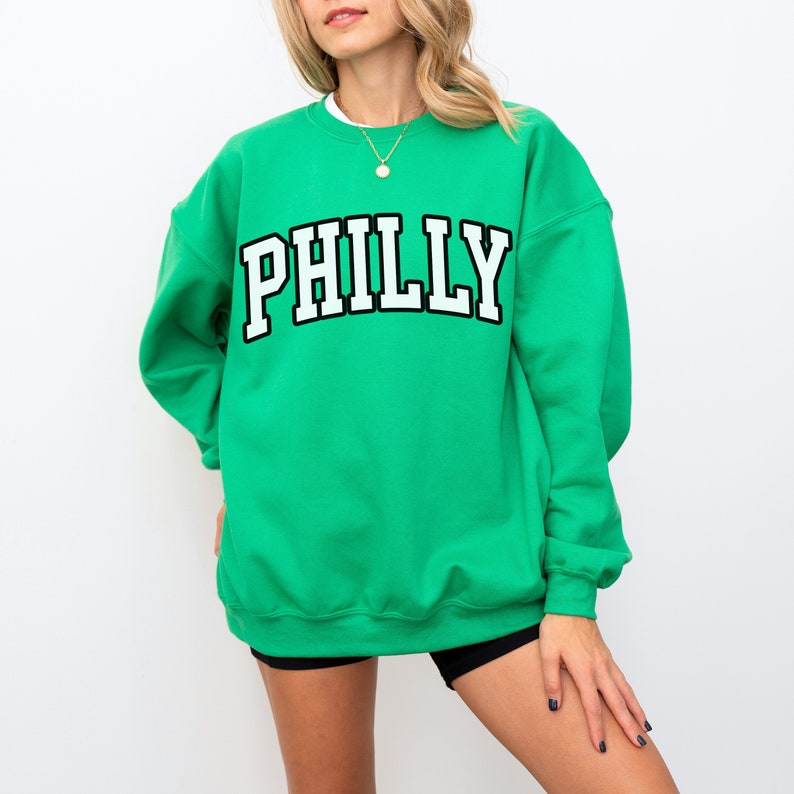 May include: A green sweatshirt with the word "PHILLY" printed in white letters with a black outline.