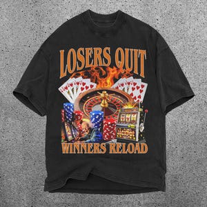 May include: Black t-shirt featuring a graphic of a casino roulette wheel, slot machine, and playing cards. The text "Losers Quit Winners Reload" is printed on the shirt.