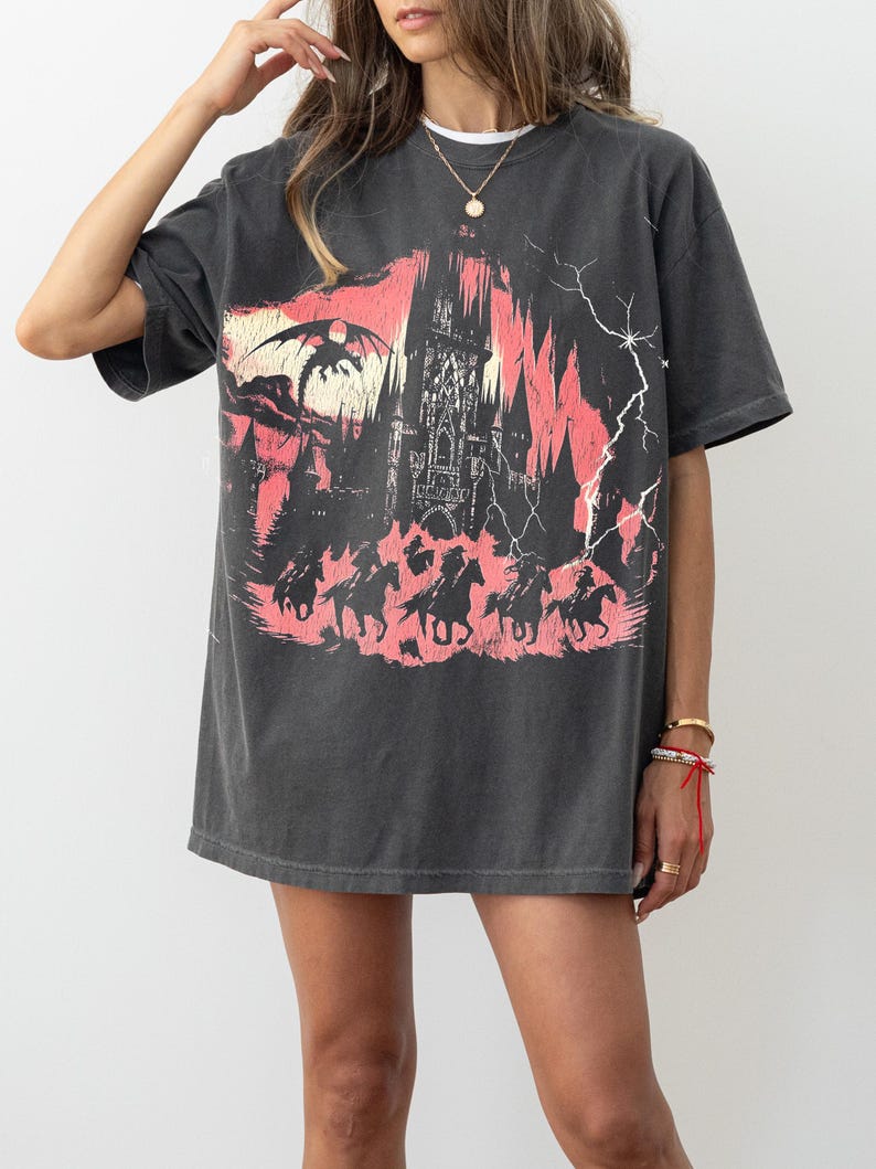 May include: A black oversized t-shirt with a graphic print of a castle, a dragon, and horses. The graphic is in shades of pink and red.