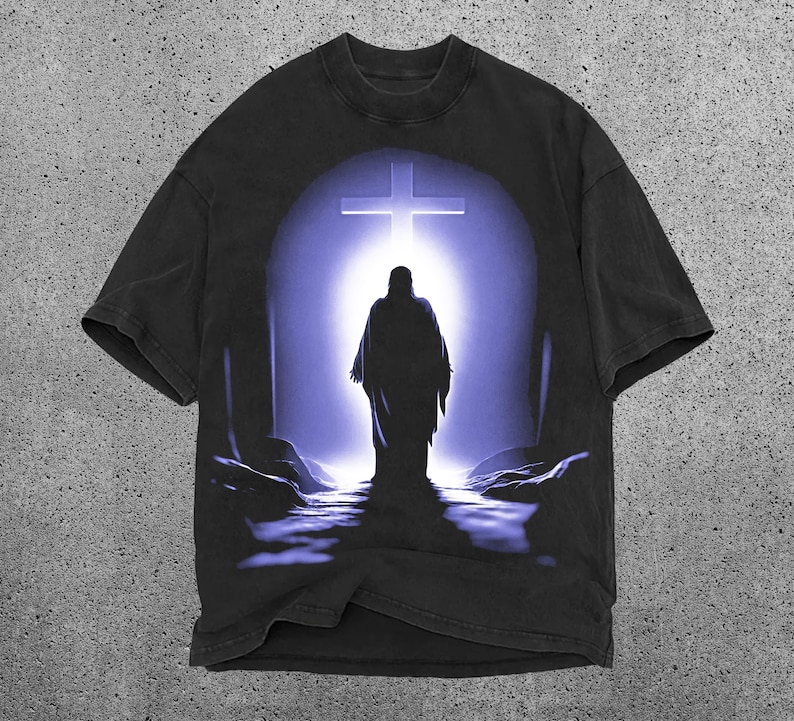 May include: Black t-shirt with a graphic print of a person walking towards a cross in a purple and blue light.