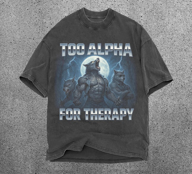 May include: Dark gray t-shirt featuring a graphic of three werewolves under a full moon with lightning. The text "TOO ALPHA FOR THERAPY" is printed above and below the image in a silver, block font. The shirt has a vintage, worn look.