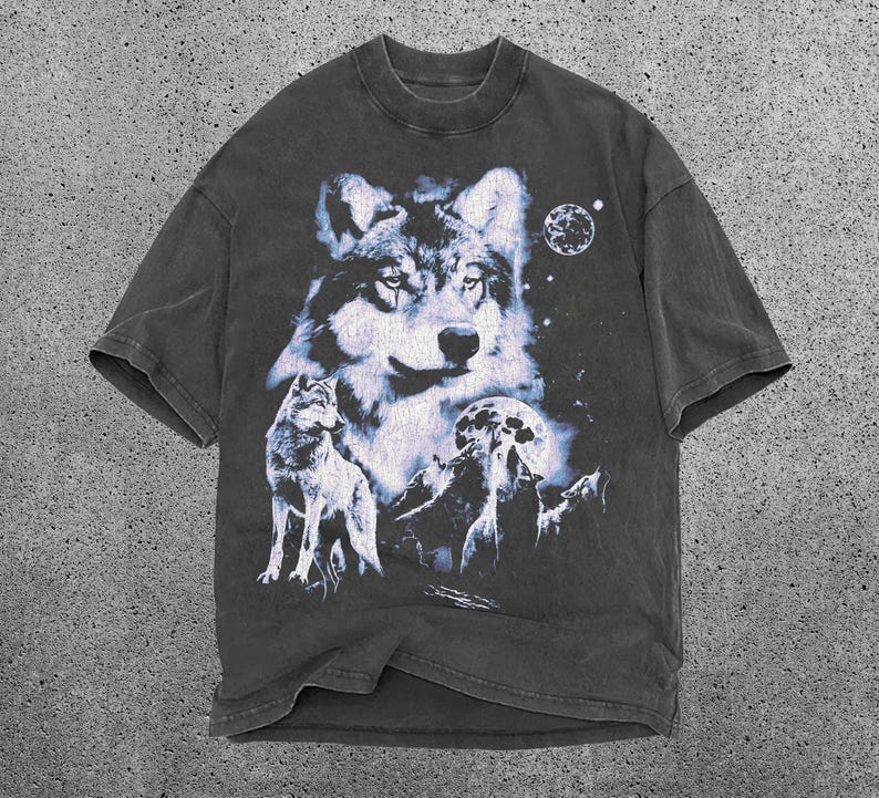 May include: Dark gray t-shirt featuring a detailed wolf graphic. The design includes a large wolf head, a smaller wolf, a full moon, and a starry night sky. The shirt has a crew neck and short sleeves.