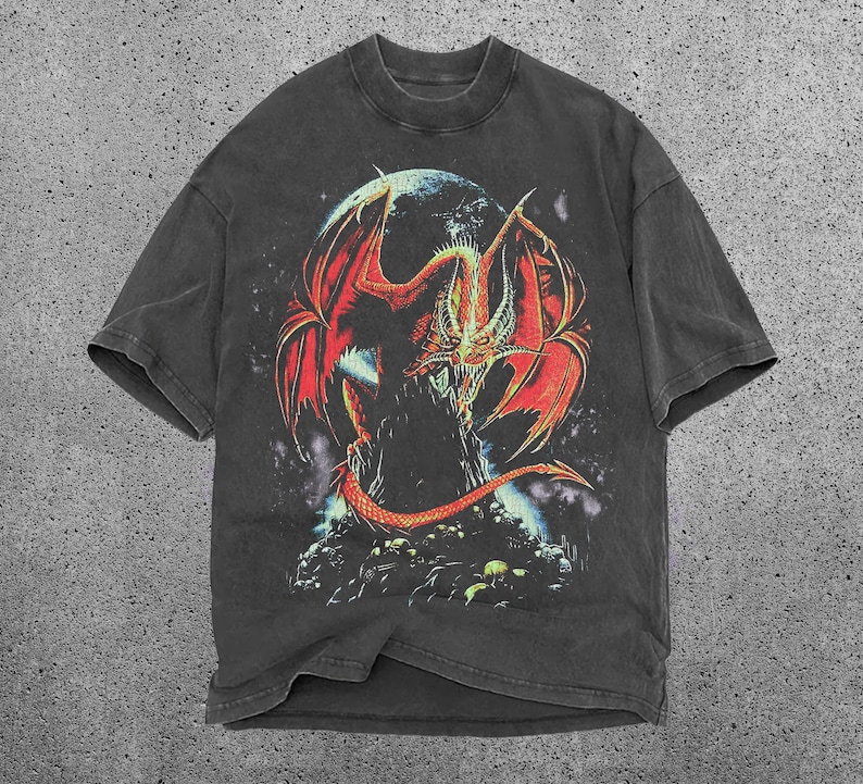 May include: Dark grey t-shirt with a striking graphic of a red and orange dragon with large wings, set against a dark background with a moon. The dragon is the focal point, with intricate scales and a menacing expression.