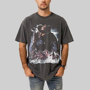 Puede incluir: Camiseta gris oscuro con un gr&aacute;fico de vaquero y caballos en el agua. El dise&ntilde;o incluye un vaquero con sombrero, con un aspecto vintage y desgastado. La camiseta es de cuello redondo y manga corta.