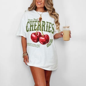 Puede incluir: Camiseta blanca con un gr&aacute;fico de dos cerezas rojas y el texto "Farm Fresh Cherries Hand Picked Nature's Candy".