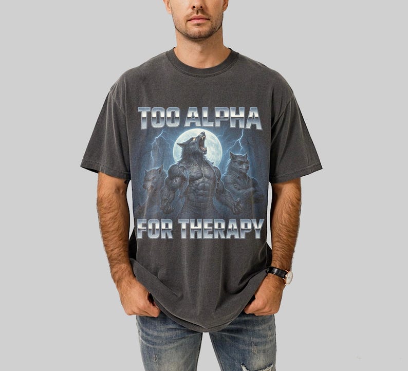 May include: Dark gray t-shirt featuring a graphic of three werewolves howling at the moon, with lightning bolts in the background. The text "TOO ALPHA FOR THERAPY" is printed above and below the graphic in a silver, metallic font.