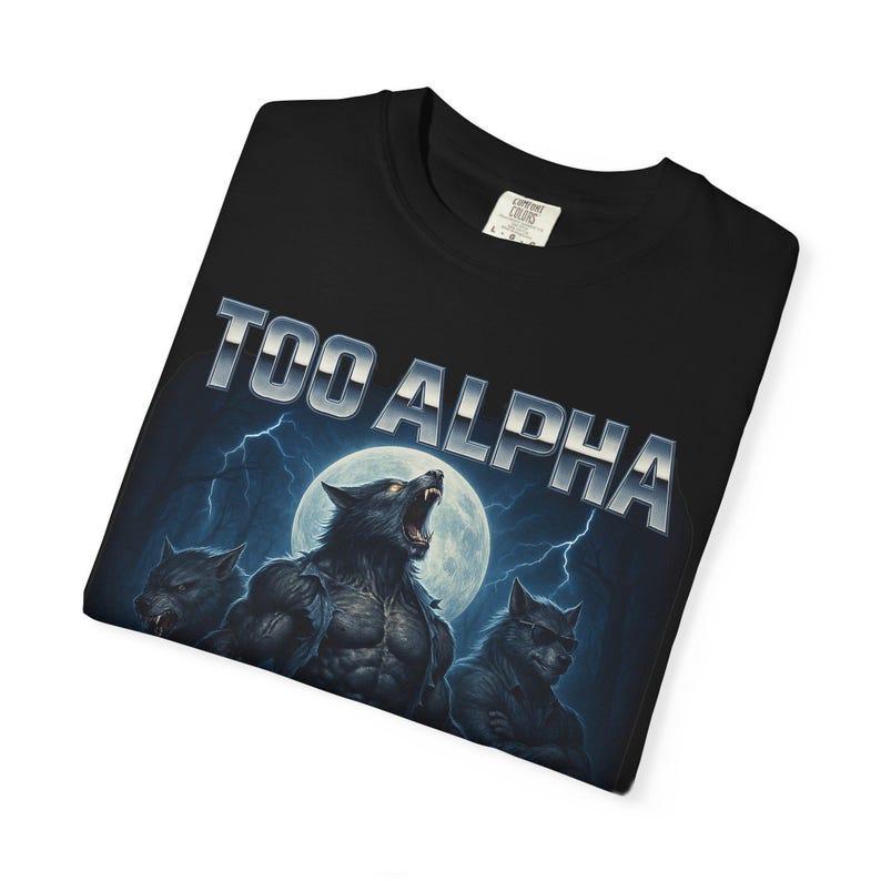 May include: Black t-shirt with the text "TOO ALPHA" in silver lettering. The graphic features three werewolves in front of a full moon and lightning bolts.