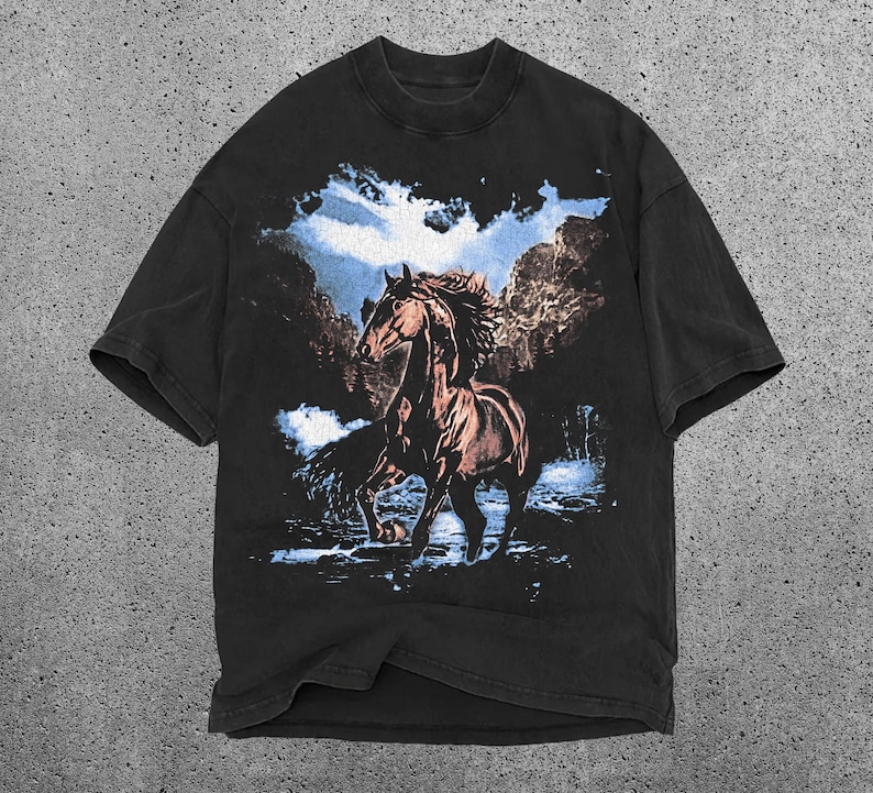 May include: Black t-shirt featuring a brown horse graphic. The horse is depicted in a running pose against a backdrop of a blue sky and trees. The shirt has a crew neck and short sleeves.