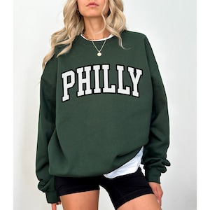 May include: A dark green sweatshirt with the word "PHILLY" printed in white with a black outline.