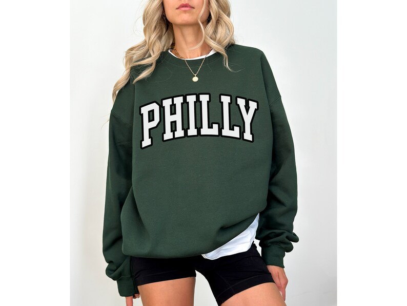May include: A dark green sweatshirt with the word "PHILLY" printed in white with a black outline.