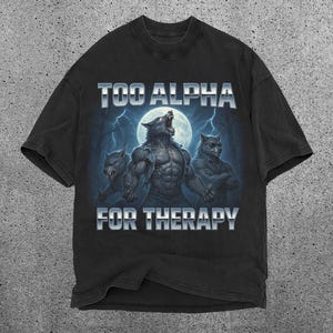 May include: Black t-shirt featuring a graphic of three werewolves under a full moon with lightning. The text "TOO ALPHA FOR THERAPY" is displayed above and below the illustration. The shirt has a vintage, distressed look.