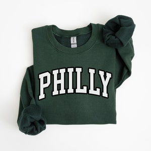 May include: A dark green sweatshirt with the word "PHILLY" printed in white with a black outline.