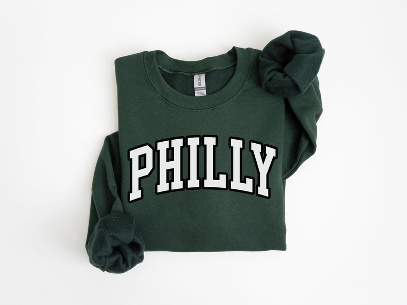 May include: A dark green sweatshirt with the word "PHILLY" printed in white with a black outline.