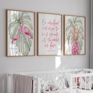 Puede incluir: Una cuna blanca con una manta rosa y almohadas decorativas se encuentra debajo de tres impresiones enmarcadas. Las impresiones presentan ilustraciones de acuarela de flamencos, plantas tropicales y texto inspirador en rosa.