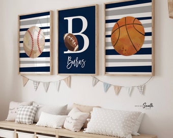 May include: Three framed wall art prints featuring sports themes. The left print shows a baseball on navy and gray stripes. The center print displays a large letter B, a football, and the text Burns. The right print features a basketball on stripes.