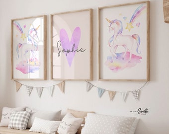 May include: Three framed watercolour prints featuring a unicorn with a rainbow and stars, a heart with the name "Sophie", and a unicorn with a rainbow and stars. The prints are hung on a white wall above a wooden bench with storage bins.