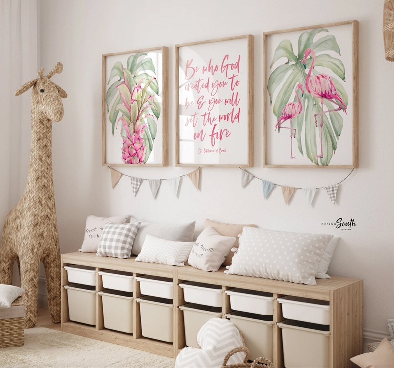 May include: Three framed watercolor prints with botanical and inspirational themes. One features a pink pineapple, another has the quote "Be who God created you to be & you will set the world on fire", and the last shows pink flamingos. The prints are displayed above a storage bench.