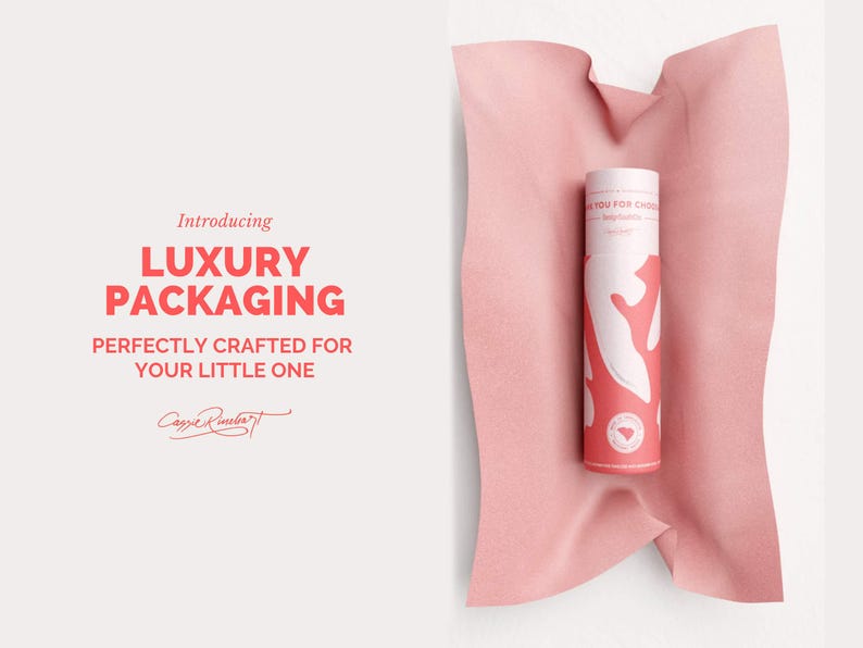 May include: A cylindrical product container with a white and coral design, resting on a pink fabric. The container has text that reads "Thank you for choosing" and "Luxury Packaging" in bold letters. The image also includes the text "Perfectly crafted for your little one."