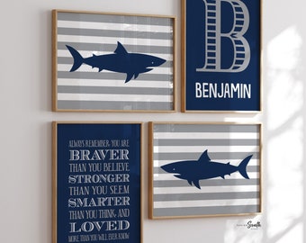 May include: Set of four framed prints with a nautical theme. The prints feature a blue shark silhouette on a grey and white striped background, a blue shark silhouette on a grey and white striped background, a blue letter B with the name Benjamin in white text, and a blue quote about being brave, strong, smart, and loved.