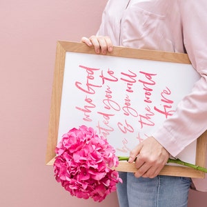 May include: Three framed prints with a tropical theme. The prints feature pink flamingos, green monstera leaves, and a pink pineapple. The center print has a pink quote that reads 'Be who God created you to be & you will set the world on fire.' The quote is attributed to St. Catherine of Siena.