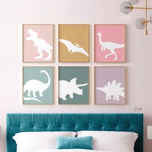 Adorable dinosaur art prints designed for a little girls room, featuring playful dinosaurs in shades of pink, teal, and purple. These vibrant and fun dinosaur illustrations are perfect for adding a touch of adventure and charm to toddler wall decor. Ideal for a girl's nursery, bedroom, or playroom, these art prints create a whimsical and colorful space. Perfect for girls who love dinosaurs, this wall decor adds personality and joy to any room setting, making it a delightful addition to her space