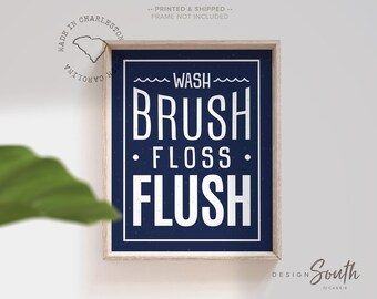 Pode incluir: Uma placa de banheiro azul marinho com texto branco que diz "Wash Brush Floss Flush". A placa é emoldurada em uma moldura de madeira clara.
