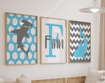 May include: Three framed prints featuring a blue and white polka dot pattern, a blue and grey chevron pattern, and a blue letter F with the name Finn on a white background. Each print includes a silhouette of a hammerhead shark.