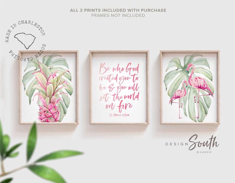 May include: Three framed prints with a tropical theme. The prints feature pink flamingos, green monstera leaves, and a pink pineapple. The center print has a pink quote that reads 'Be who God created you to be & you will set the world on fire.' The quote is attributed to St. Catherine of Siena.