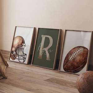 May include: Three framed wall art prints featuring a watercolour illustration of a brown football helmet, a large letter R on a dark green background with cursive text, and a brown football. The prints are displayed in light wood frames.