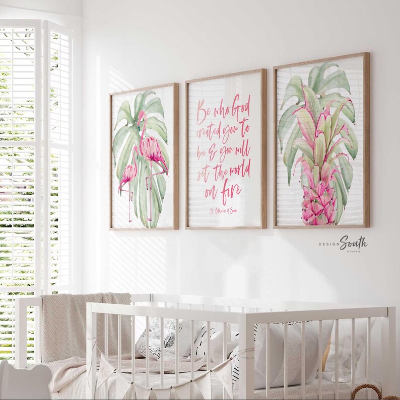 May include: Three framed prints with a tropical theme. The prints feature pink flamingos, green monstera leaves, and a pink pineapple. The center print has a pink quote that reads 'Be who God created you to be & you will set the world on fire.' The quote is attributed to St. Catherine of Siena.