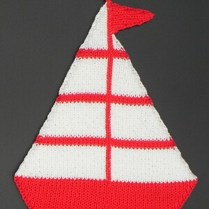 Puede incluir: Un agarrador de cocina tejido en forma de velero. El agarrador es principalmente blanco con rayas rojas y una base roja. Una pequeña bandera roja está unida en la parte superior. El agarrador tiene un lazo para colgar.