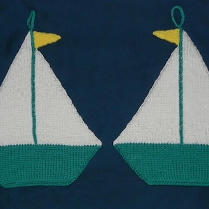 Könnte beinhalten: Zwei handgestrickte Topflappen in Form von Segelbooten. Jedes Boot hat ein weißes Segel, einen grünen Rumpf und eine gelbe Flagge. Die Topflappen sind vor einem dunkelblauen Hintergrund platziert, für Küchen mit nautischem Thema.