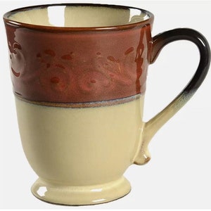 May include: A brown and cream ceramic mug with a decorative design. The mug has a wide base and a handle.