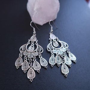 May include: A pair of silver dangle earrings with intricate filigree designs. The earrings feature multiple teardrop-shaped pendants and a circular design at the top.