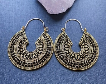 May include: A pair of gold hoop earrings with a black filigree design. The earrings are large and have a circular shape.