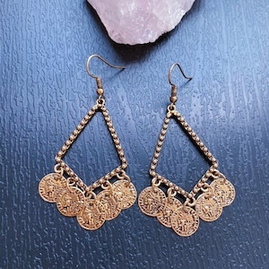 May include: Gold tone dangle earrings with a triangle shape and multiple coin-shaped charms.