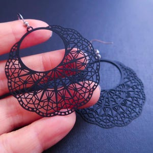 May include: A pair of black metal earrings with a delicate, intricate, circular design. The earrings are lightweight and have a modern, geometric look.