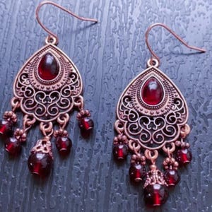 May include: A pair of dangle earrings with a filigree design and red gemstone accents.