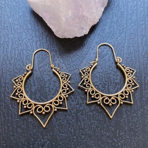 May include: A pair of gold hoop earrings with a delicate, intricate design. The earrings are shaped like a sun with a circular center and radiating points.