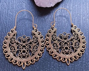 May include: A pair of gold-colored filigree earrings. Each earring features a crescent-shaped design with intricate scrollwork and a long, curved hook for the ear. The earrings have a vintage or bohemian aesthetic.