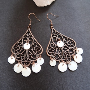 May include: A pair of dangle earrings with a filigree design and white shell accents. The earrings are made of copper and have a vintage look.
