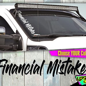 May include: A white pickup truck with a black light bar on the roof. The truck has a white decal on the windshield that says "Financial Mistake".