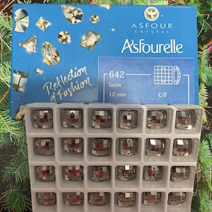 May include: A clear plastic container with 24 silver square-shaped rhinestones. The container is labeled "Asfour Crystal" and "642 Satin 12 mm C/F".